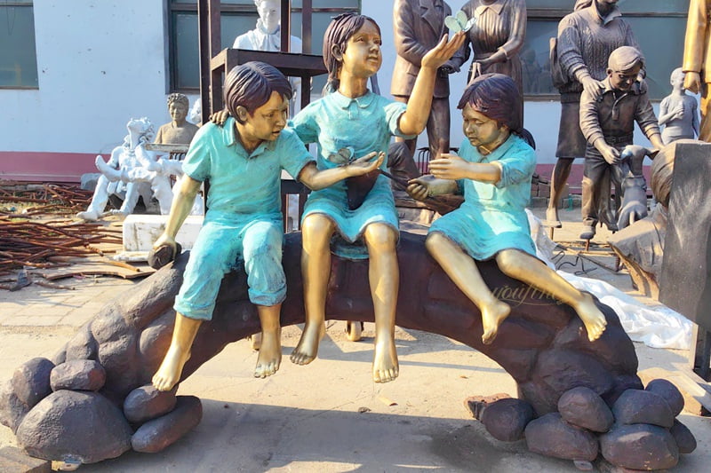 Statues of a boy and girl playing with a butterfly on a tree stump