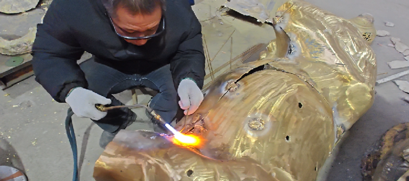 Craftsman performing TIG welding on bronze sculpture in workshop