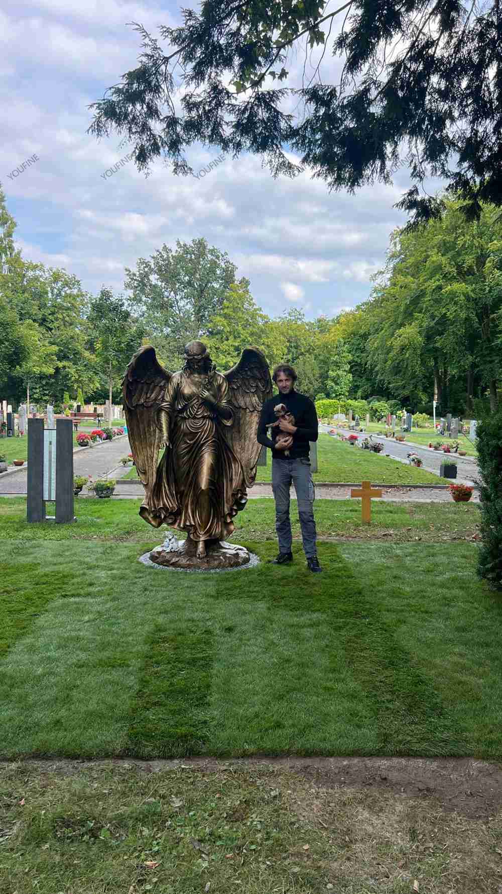 Bronze angel statue in a cemetery garden with a visitor nearby