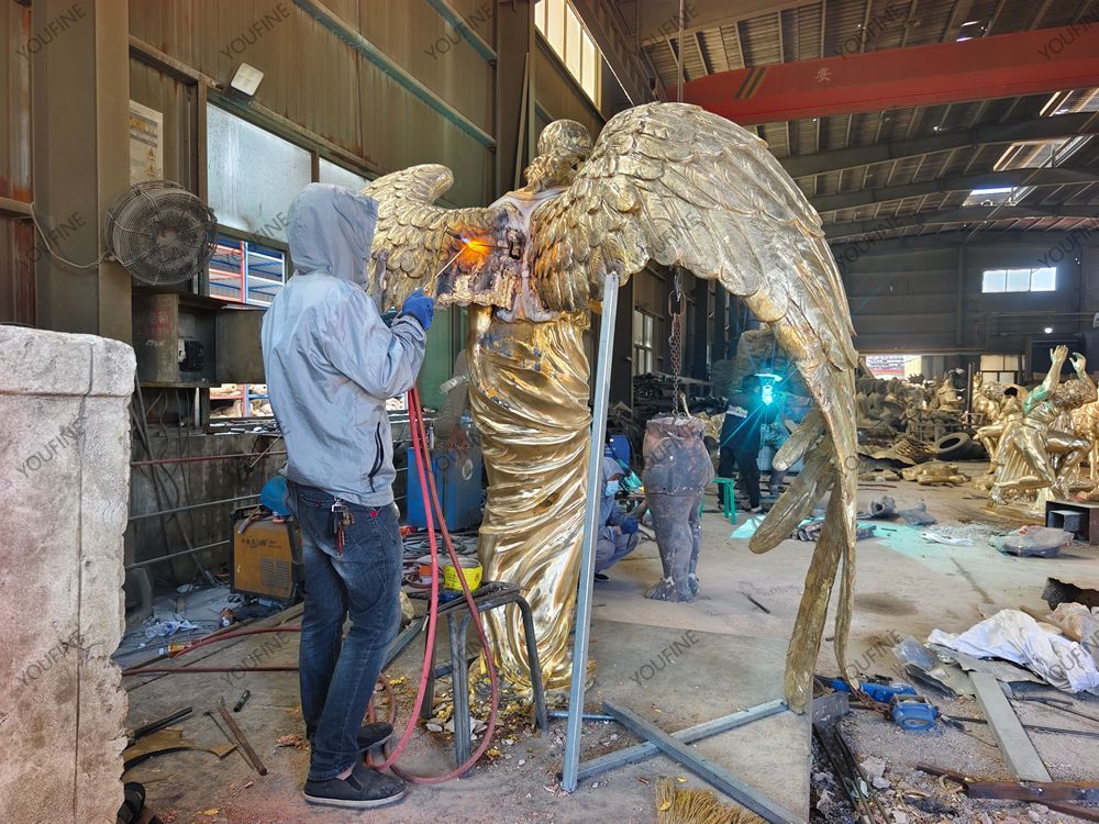 Foundry craftsperson welding the wing section of a bronze angel statue