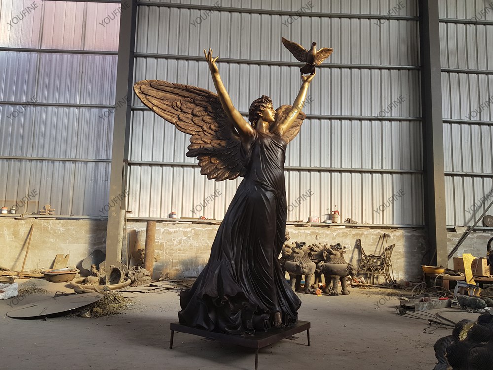Large bronze angel statue with raised arms and dove in the YouFine factory